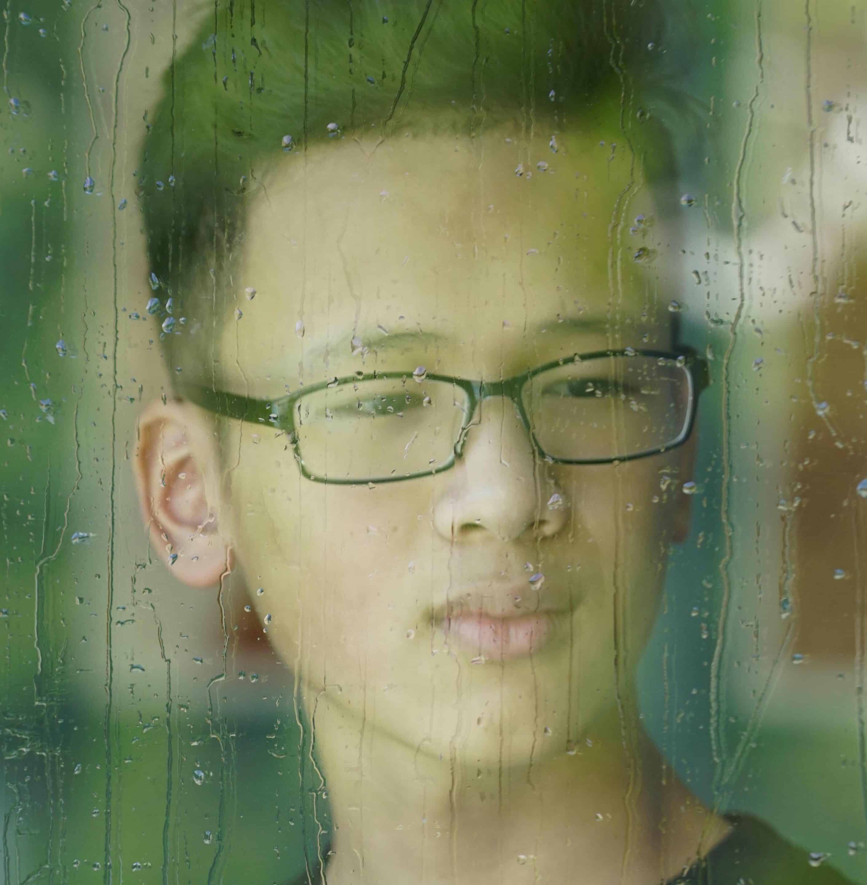 Image of young Asian person, looking out the window. 