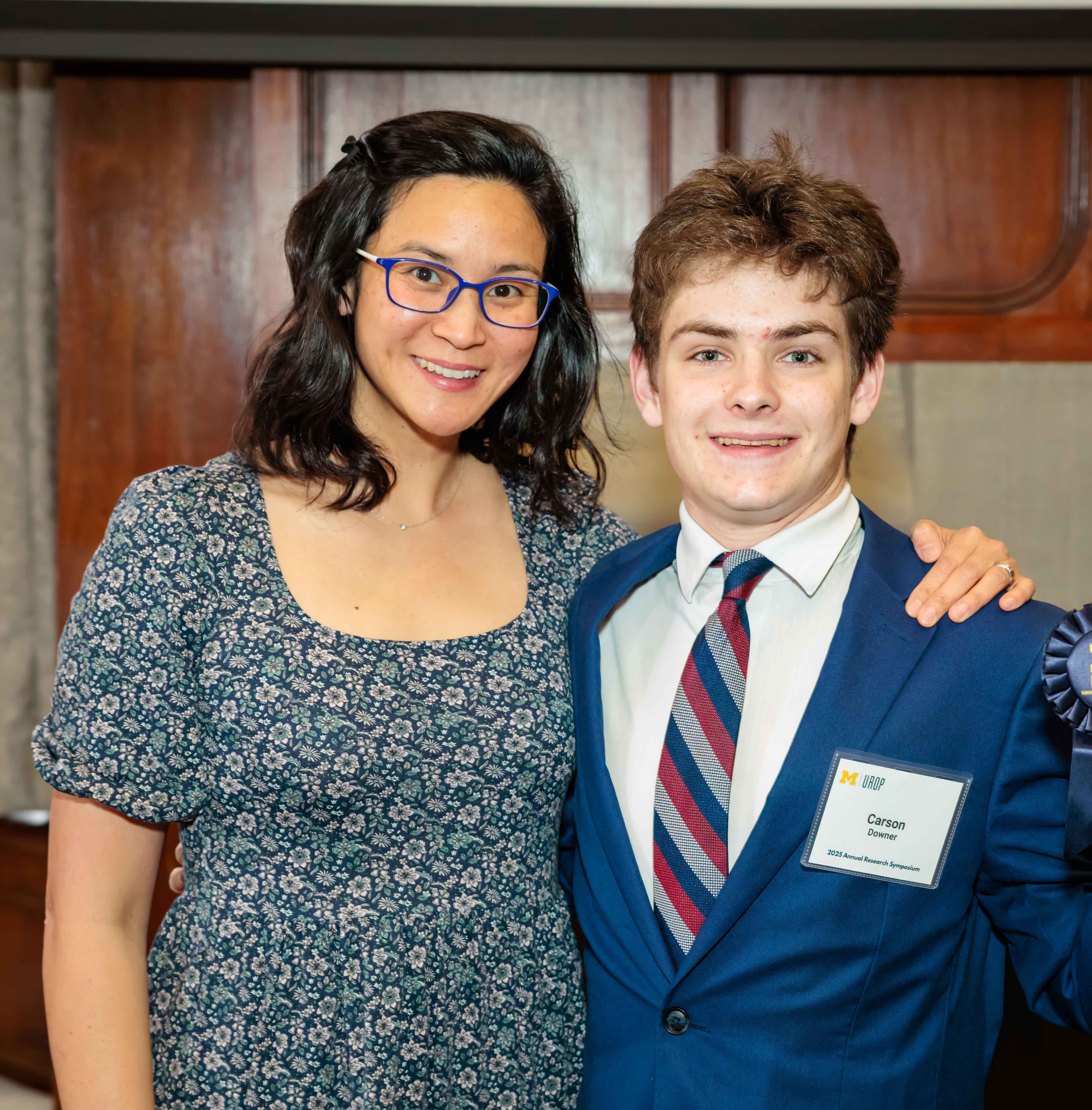Group photo showing, from left to right, University of Michigan student Carson Downer, a young man in a navy blazer and tie; Dr. Tammy Chang, a woman with dark hair and glasses, wearing a grey sweater, and University of Michigan student Aamina Hussein, a young women with dark hair, wearing a blue-grey jacket, pictured in front of two research posters.
