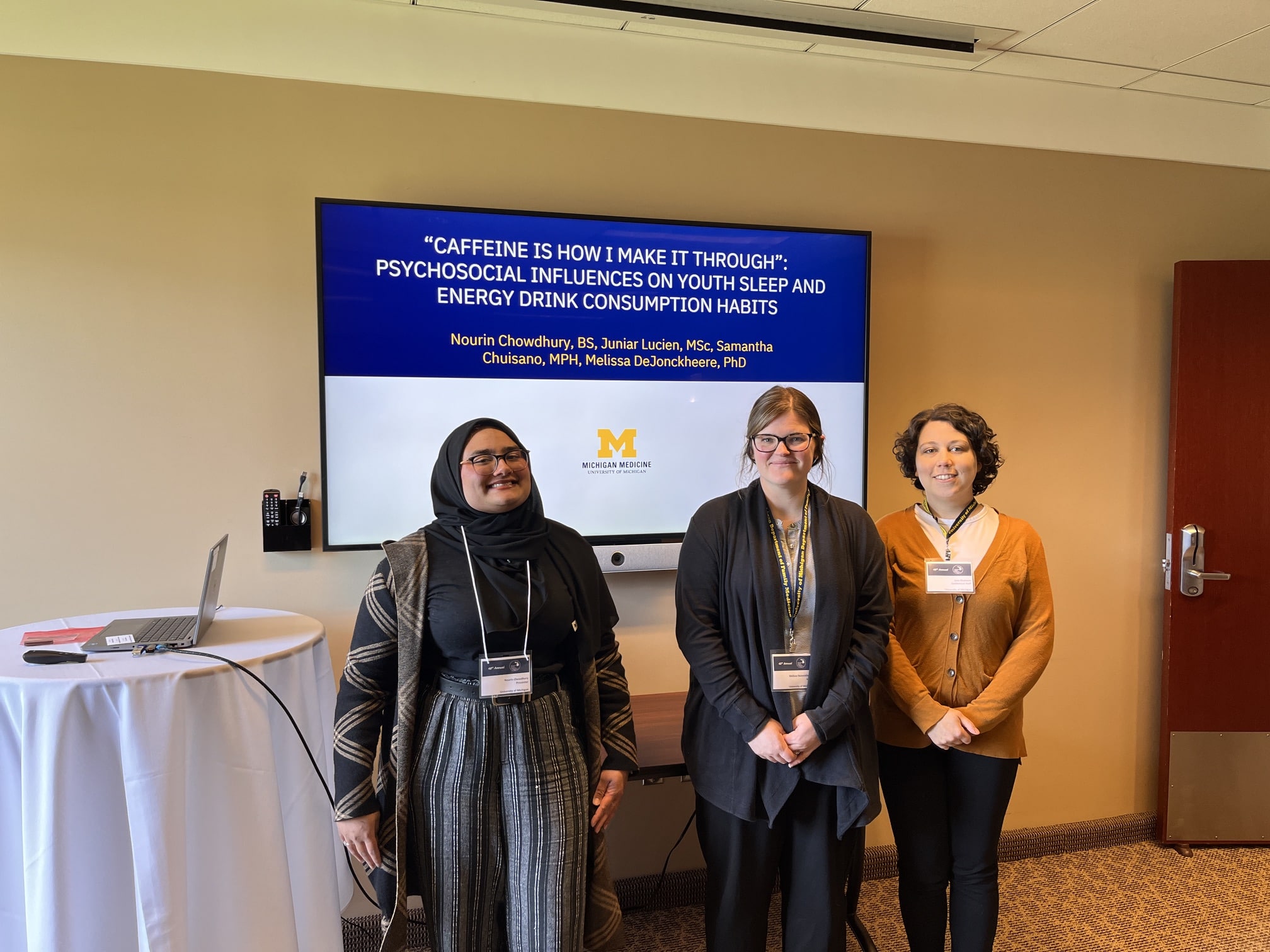 Three women of varying races and ages, including from left to right, Nourin Chowdhury, Melissa DeJonckheere, and Sam Chuisano, in front of a research poster.
